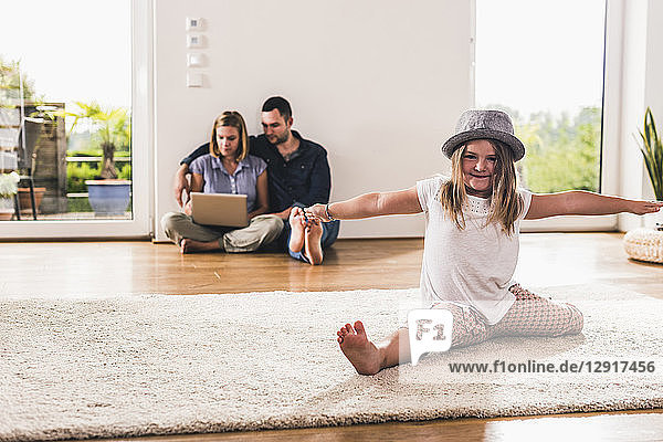 Little girl with hat having fun at home  parents using laptop in background