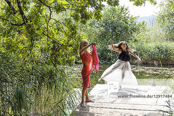 Two girls on jetty at a pond in fancy dresses