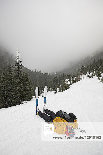 Totale Aufnahme eines müden Skifahrers  der im Schnee liegt