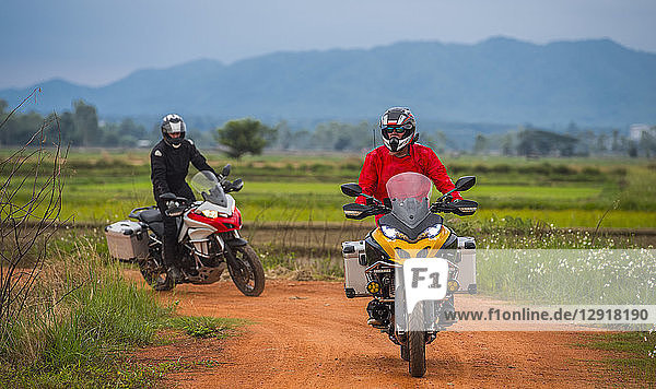 Zwei Männer auf Motorrädern auf einer leeren Schotterstraße mit einem Hügel im Hintergrund  ¬ÝChiang¬ÝMai  ¬ÝMueang¬ÝChiang Mai District  Thailand