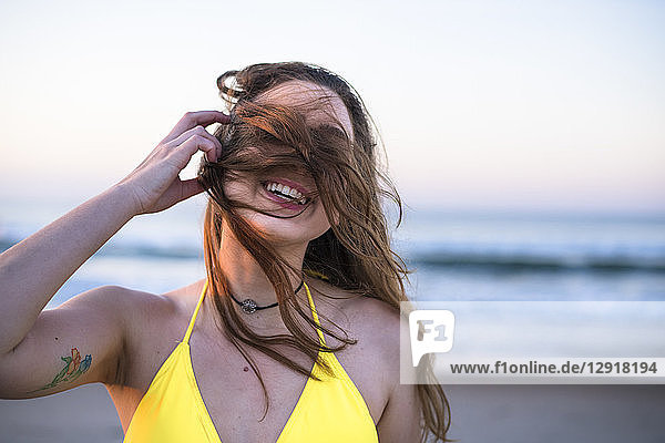 Kopf- und Schulteraufnahme einer lächelnden Frau im gelben Bikini am Strand mit vom Wind zerzaustem Haar