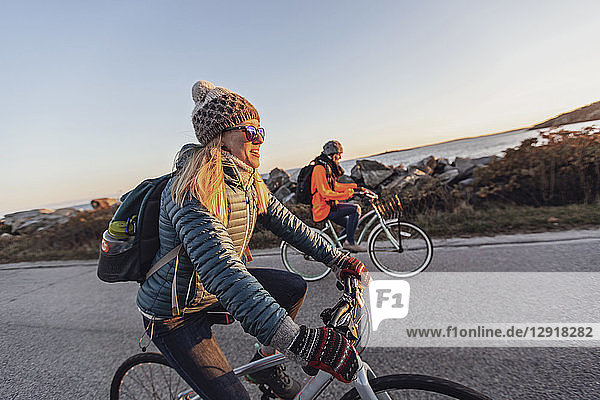 Two female friends cycling together along coastal road at dusk  Portland  Maine  USA