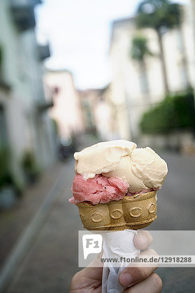 Hand hält Eiswaffel mit zwei Eissorten und Altstadt im Hintergrund  Locarno  Tessin  Schweiz