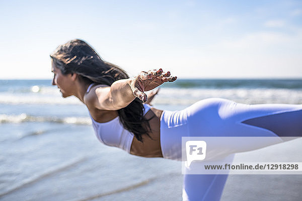 Seitenansicht einer jungen Frau  die auf einem Bein steht und die Arme ausstreckt  während sie am Strand Yoga macht