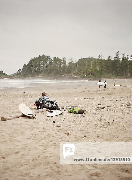 Surfer sitting on log on sandy beach  Vancouver  British Columbia  Canada