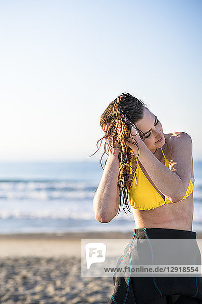Waist up shot of woman in yellow bikini on beach with hands in hair