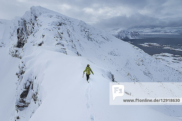 Distant view of single female hiker ascendingÂ MatmoraÂ mountain peak in winter  Â Austvagoy  Â LofotenÂ Islands  Norway
