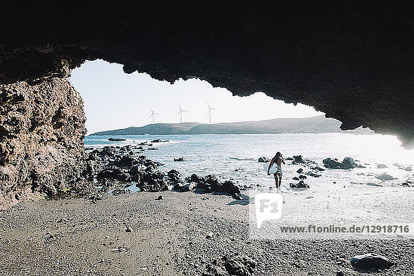 Blick aus einer Höhle auf eine Surferin im Bikini  die mit ihrem Surfbrett am Strand spazieren geht  Teneriffa  Kanarische Inseln  Spanien
