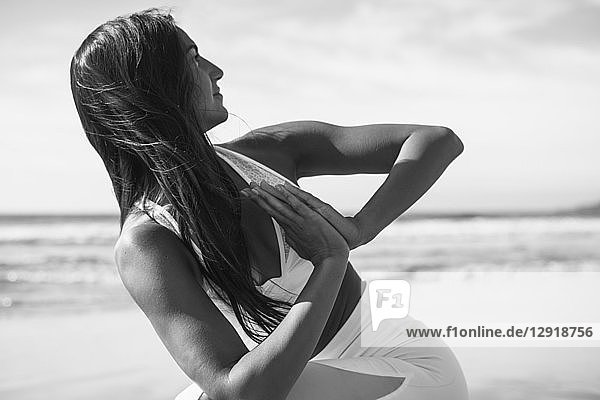 Foto einer jungen Frau  die am Strand mit verschränkten Händen Yoga macht