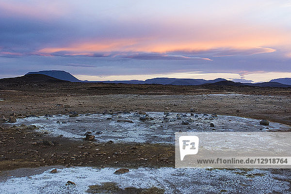 Blue coloured minerals left behind by volcanic mud puddles and fumes contrast with the orange coloured sky in Hverarˆšˆ‚ndor Hverir Geothermal Area at Namaskard Pass North Iceland.