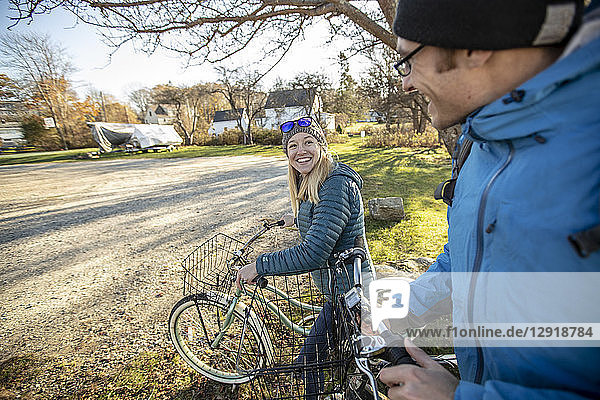 Lächelndes junges Paar beim Spaziergang mit Fahrrädern durch ein Dorf im Herbst  Portland  Maine  USA