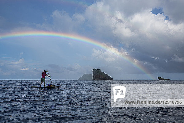 Side view of man paddleboarding in sea under rainbow Misool Raja Ampat Indonesia