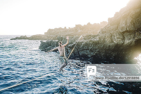 Junger Mann ohne Hemd balanciert auf einem Drahtseil über einem Küstengewässer ¬ÝTeneriffa  Kanarische Inseln  Spanien