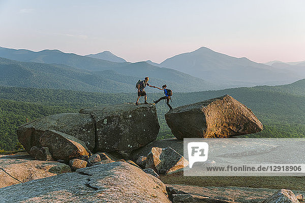 Fernansicht eines Mannes  der einer Frau beim Wandern über einen Felsbrocken hilft  Pitchoffâ€ Mountain  Adirondack Mountains  New York State  USA