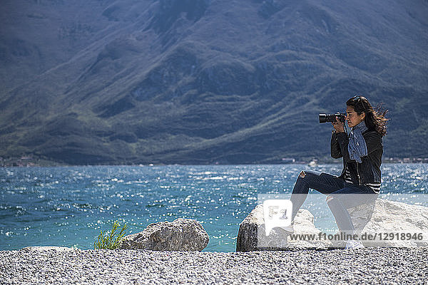 Frau sitzt auf einem Felsen an der Küste und fotografiert den Gardasee  Verona  Italien