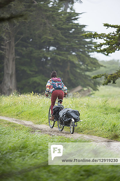 Young adult woman riding on bike through grassy area towing small trailer   Santa Cruz  California  USA