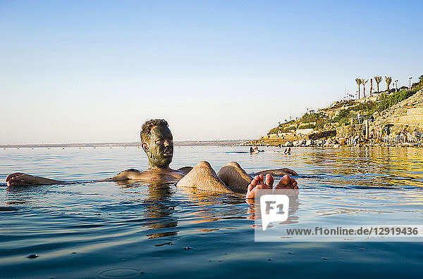 Man with mud on face floating in Dead Sea  Madaba Governorate  Jordan