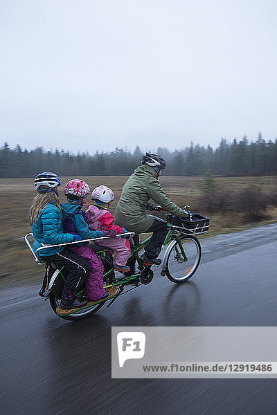 Mutter fährt mit ihren drei Mädchen auf dem Fahrrad von zu Hause zur Schule im Regen  Sandpoint  Idaho  USA