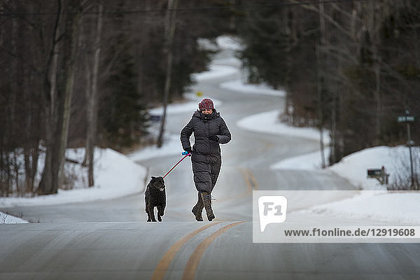 Front view of mature woman walking with dog along road in forest in winter