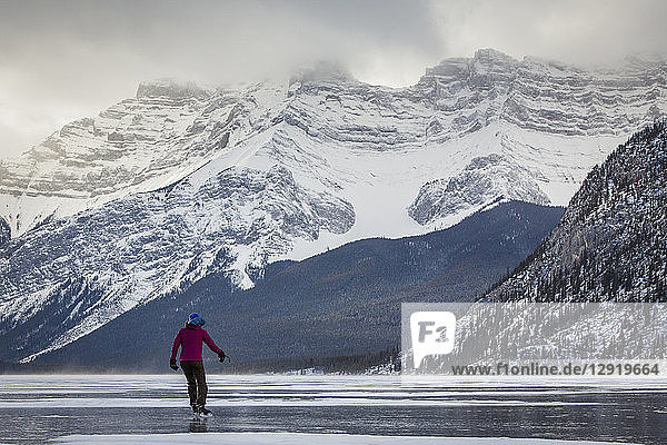 Rückansicht einer Frau beim Schlittschuhlaufen auf dem zugefrorenen Lake Minnewanka im Winter  Banff National Park  Alberta  Kanada