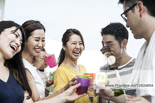 Gruppe fröhlicher junger japanischer Männer und Frauen  die im Freien stehen und mit Plastikbechern anstoßen.