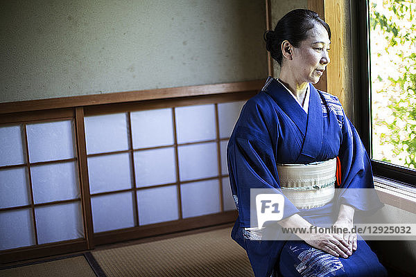 Japanische Frau in traditionellem hellblauem Kimono mit cremefarbenem Obi auf dem Boden kniend in traditionellem japanischen Haus.