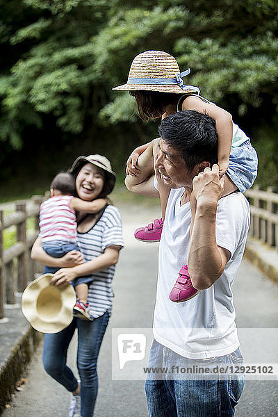 Japanisches Mädchen  lächelnde Frau mit Hut und Mann  der ein Kleinkind auf den Schultern trägt  auf Holzbrücke stehend.