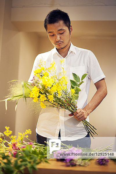 Japanischer Mann in einer Blumengalerie  der an einem Ikebana-Arrangement arbeitet.