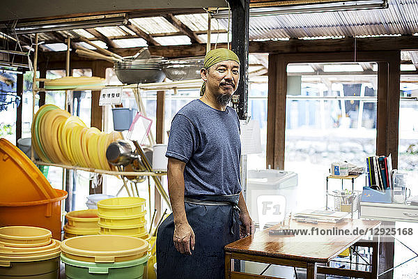 Japanischer Mann mit Kopftuch  der in einer Färberei für Textilpflanzen steht und in die Kamera lächelt.