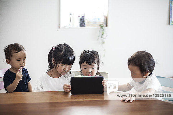 Four young Japanese children sitting at a table  looking at digital tablet.