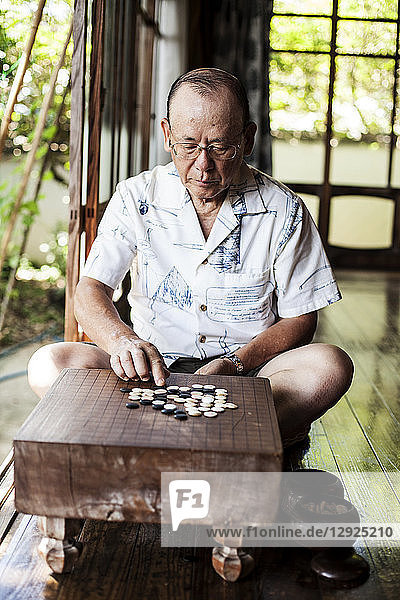 Japanischer Mann sitzt auf dem Boden auf der Veranda eines traditionellen japanischen Hauses und spielt Go.