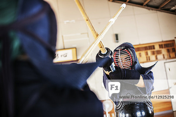 Two Japanese Kendo fighters wearing Kendo masks practicing with wood sword in gym.