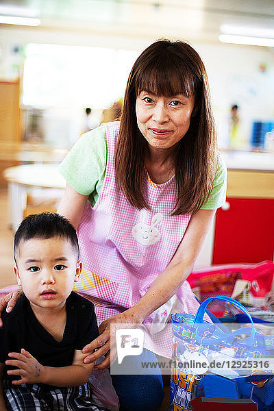 Female teacher and boy in a Japanese preschool  smiling at camera.