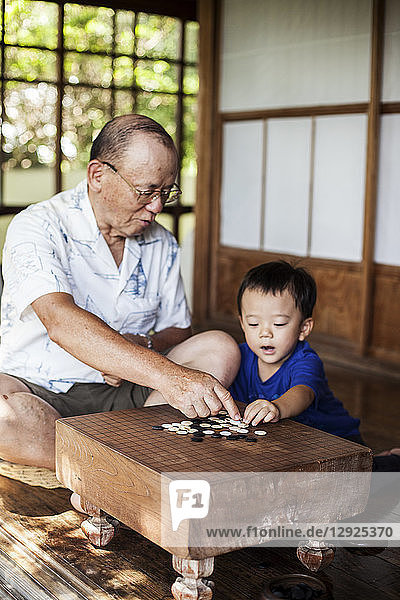 Japanischer Mann und kleiner Junge sitzen auf dem Boden auf der Veranda eines traditionellen japanischen Hauses und spielen Go.