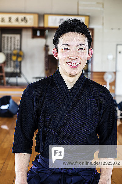 Männlicher japanischer Kendo-Kämpfer steht in einer Turnhalle und lächelt in die Kamera.