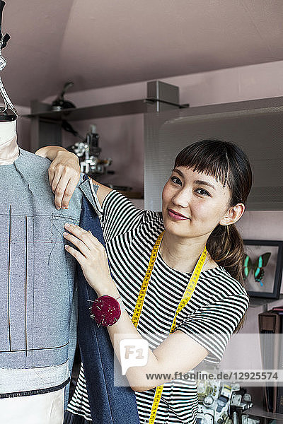 Japanische Modedesignerin  die in einem Atelier an einem Kleidungsstück nach dem Modell einer Schneiderin arbeitet.