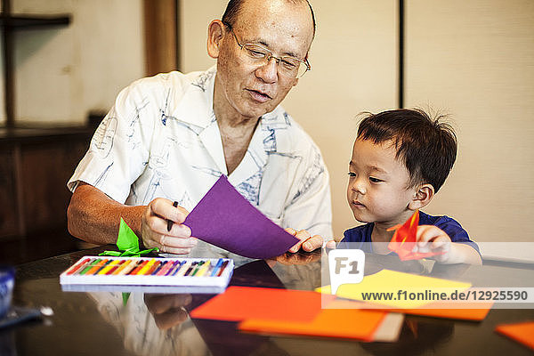 Japanese man and little boy sitting at a table  making Origami animals using brightly coloured paper.