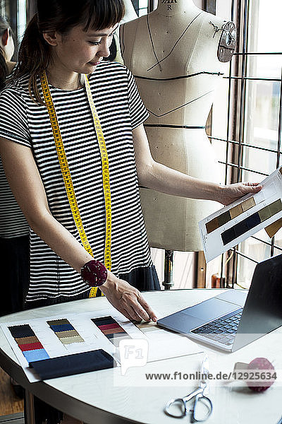 Japanese female fashion designer working in her studio  looking at fabric samples  using laptop.