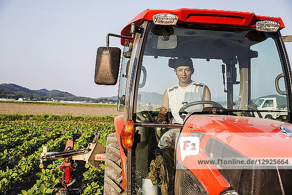 Portrait of Japanese farmer driving red tractor.
