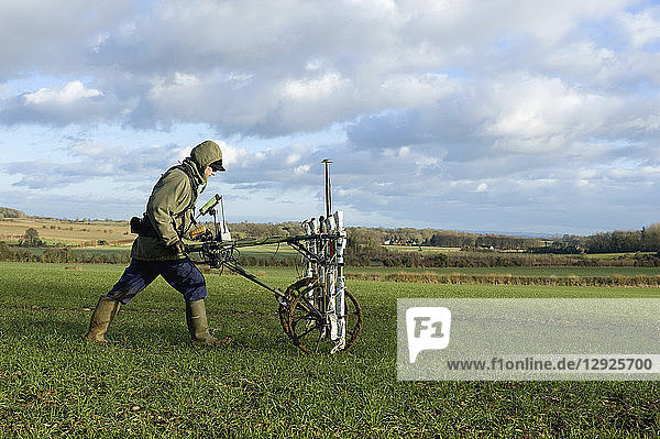 A geophysicist pushing a trolley with ground mapping sensors  creating a geophysical survey of the subsoil in a field.