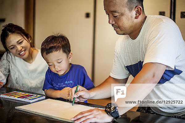 Japanese woman  man and little boy sitting at a table  drawing with colouring pens.