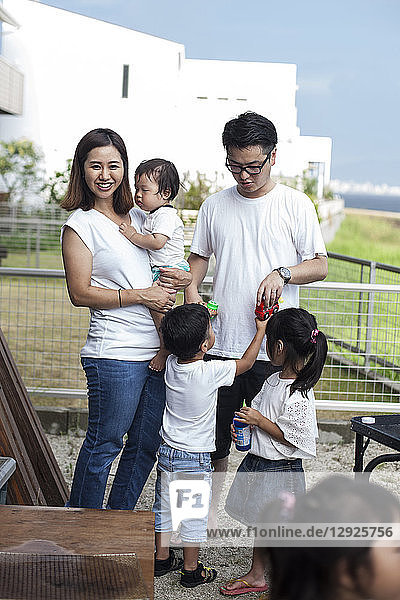 Porträt einer lächelnden japanischen Familie mit drei kleinen Kindern  die in einem Garten hinter dem Haus stehen.