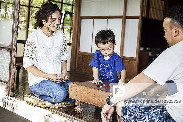 Japanische Frau  Mann und kleiner Junge sitzen auf dem Boden auf der Veranda eines traditionellen japanischen Hauses und spielen Go.