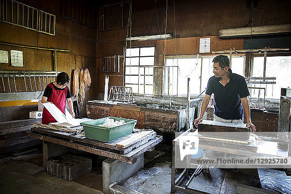 Zwei Personen  Mann und Frau  die traditionelles Washi-Papier herstellen. Schalen mit Zellstoff- und Holzrahmen und Trockengestelle.