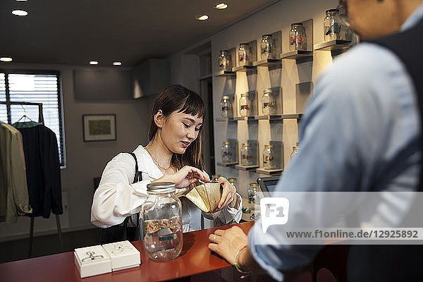 Smiling Japanese woman standing at counter in clothing store  paying with credit card.