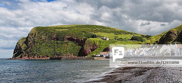 Stone beach and row of white houses of Pennan coastal fishing village on North Sea in Aberdeenshire Scotland UK with Black Hill sea cliff.