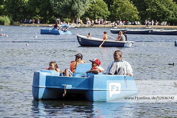 United Kingdom Great Britain England  London  Royal Parks  Hyde Park  green space  The Serpentine  recreational lake  pedal paddle boat  Black  man  girl  boy  child  family  father  son  saughter  life jacket vest  flotation device  safety