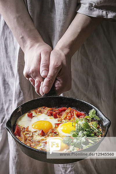 Traditional Israeli Cuisine dishes Shakshuka (Fried egg with vegetables tomatoes and paprika in cast-iron pan in female hands)
