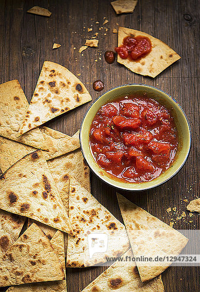 Kleine Schale und Tomatensalsa  serviert mit handgemachten Tortilla-Chips auf einem rustikalen Holzbrett