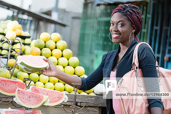 Eine lächelnde junge Frau greift auf einem Straßenmarkt nach einer Scheibe reifer Früchte.